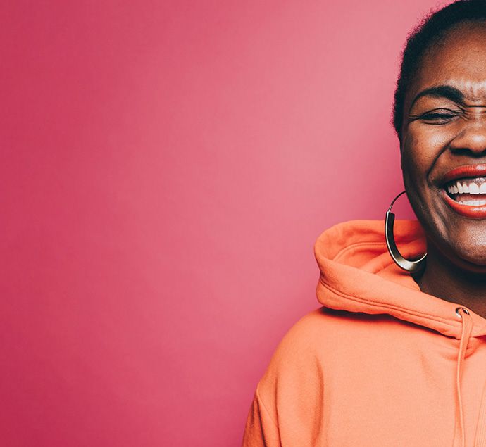 BAME female in her late 50s wearing an orange hoodie standing against a pink background