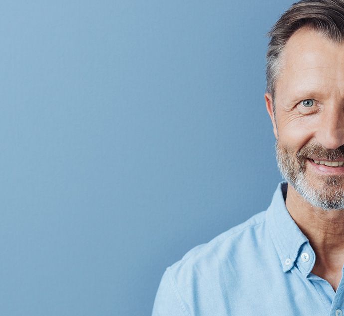 Male in his early 50s wearing a blue shirt standing against a pale blue background